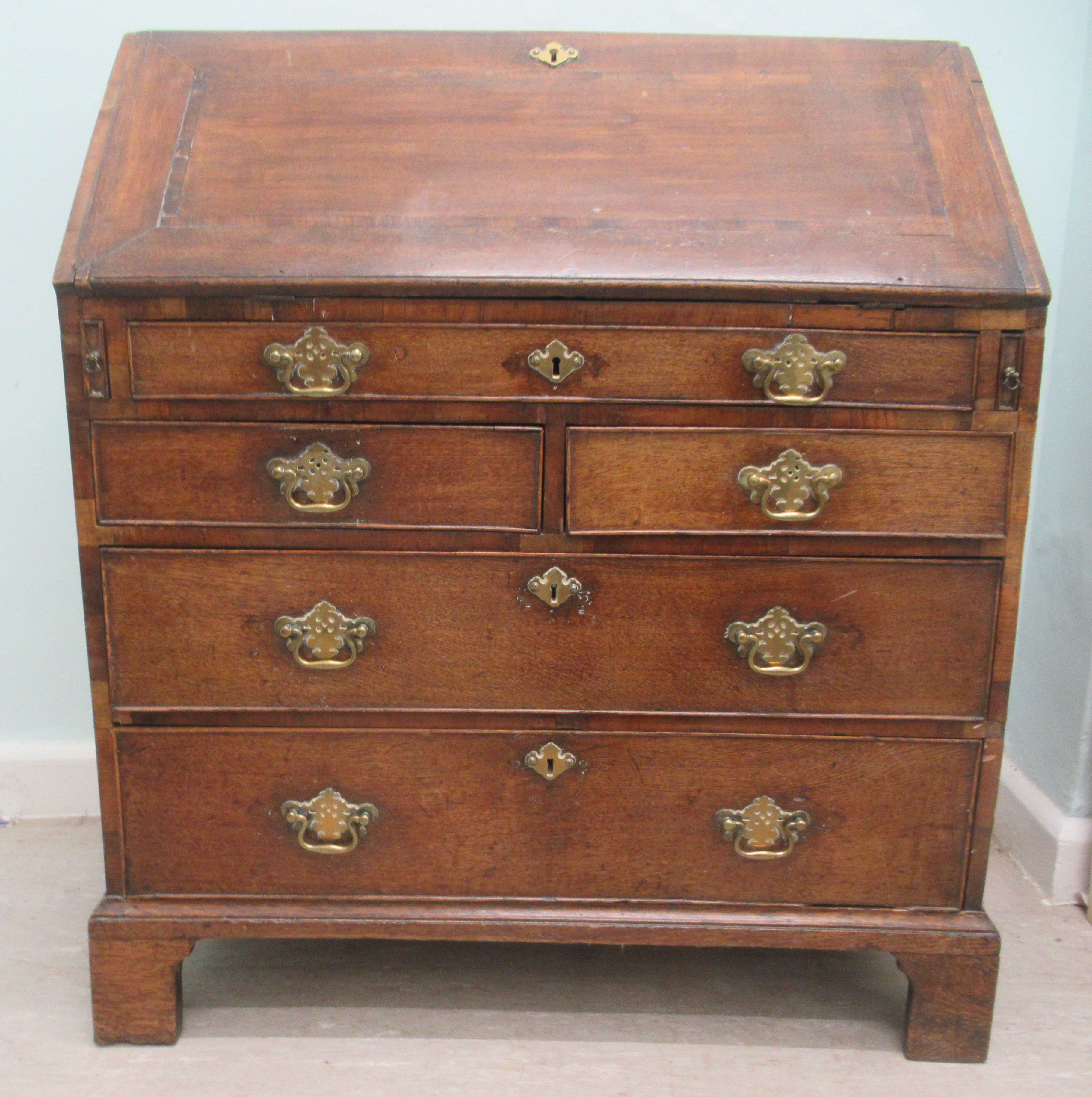 A George III oak bureau, the fall flap over an arrangement of five drawers, raised on bracket