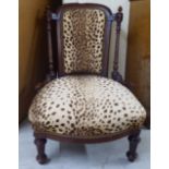 An Edwardian walnut framed nursing chair, later upholstered in leopard print fabric, raised on