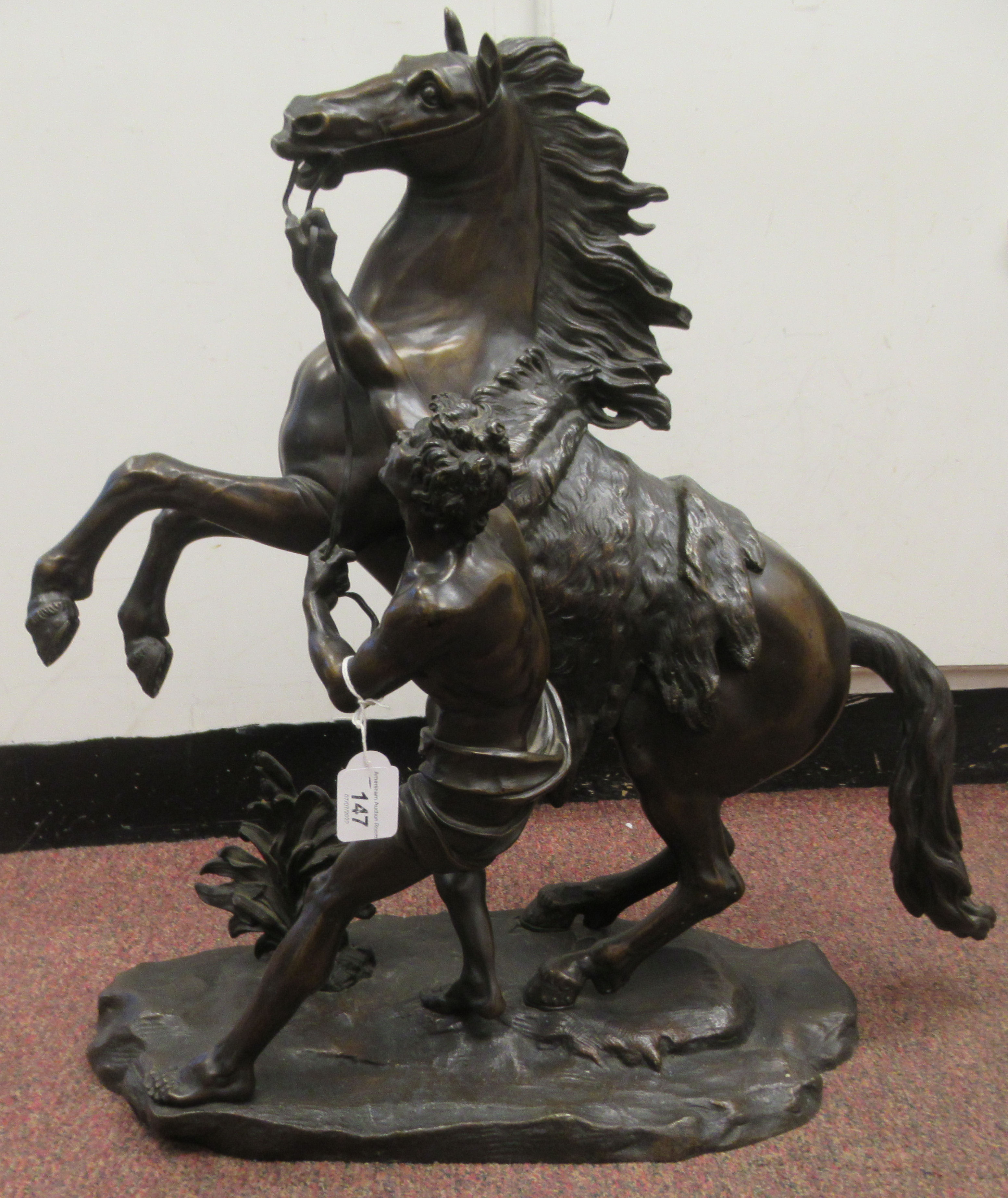 After Guillaume Couston - a cast and patinated bronze statue, a Marly horse and attendant  23"h