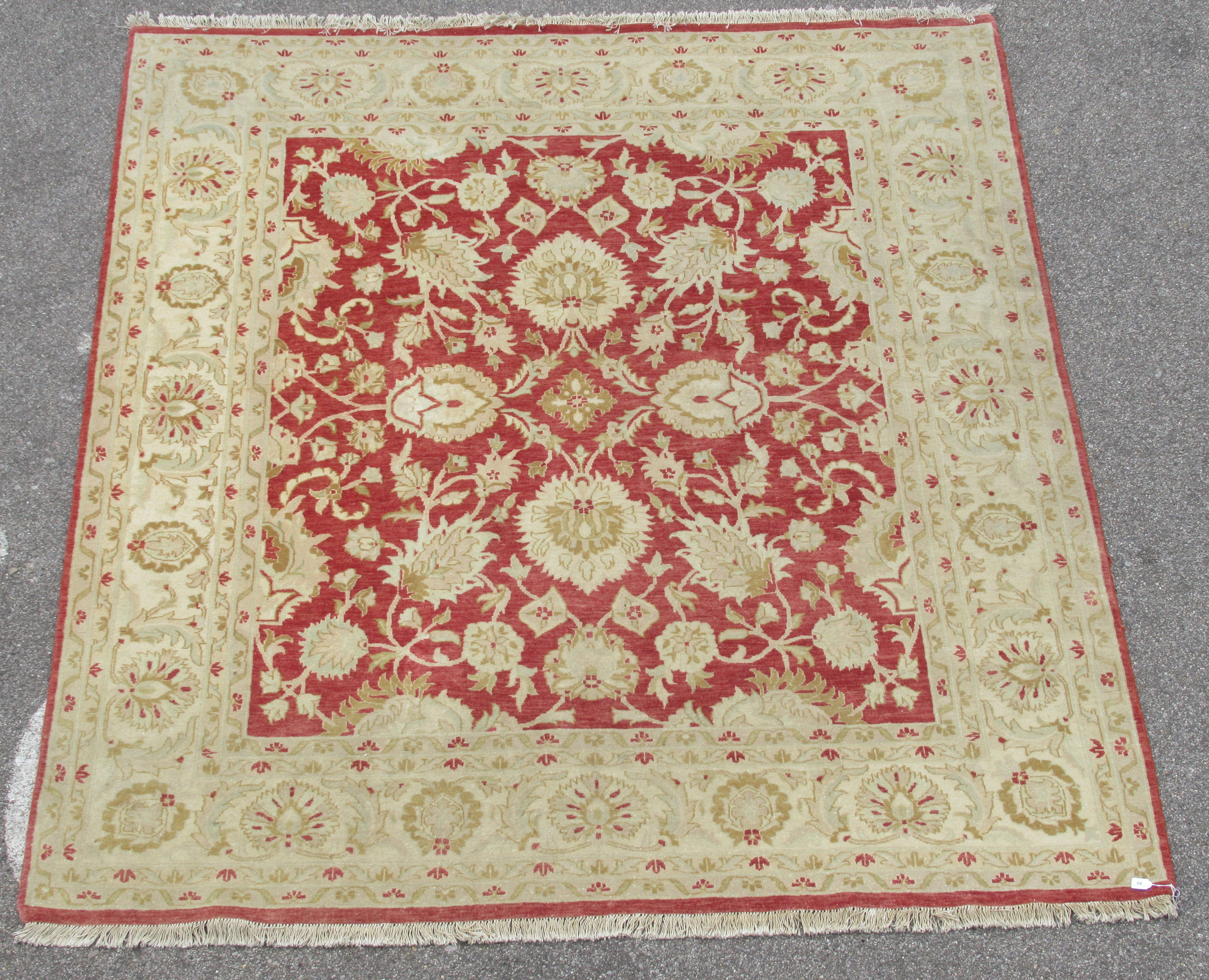 A Persian carpet, decorated with repeating stylised floral designs, on a cream and salmon coloured