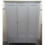 A modern grey painted three door wardrobe, enclosing a hanging rail and an open shelved interior,