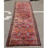 A Persian runner, decorated with stylised designs, on a red ground  33" x 128"