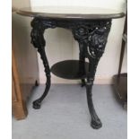 An early 20thC black painted cast iron pub table with mask ornament and a turned stained oak top