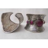 A silver coloured metal bangle of textured form, set with five ruby coloured stone tablets; and