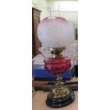 An early 20thC oil lamp with a clear glass funnel and shade, over a cranberry coloured glass