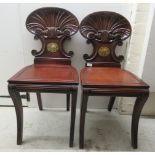 A pair of Regency mahogany framed hall chairs, each having a waisted, scroll and shell carved back