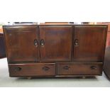 An Ercol dark stained elm sideboard with three doors, over two inline drawers, on a plinth and