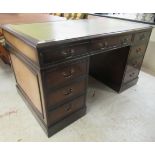A modern stained mahogany finished nine drawer, twin pedestal desk with a tooled and gilded green