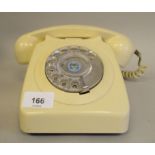 A cream coloured plastic cased telephone with a rotating dial, in a cradle