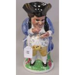 An early 19thC Staffordshire pottery Toby jug, a portly gentleman wearing a tricorn hat, a blue coat