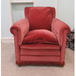 A 20thC dusky pink upholstered enclosed armchair with a rounded scrolled back on casters