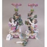 A pair of 19thC porcelain candlesticks, featuring a floral socket, surmounted by a cherubic figure