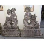 A pair of composition stone, two part terrace ornaments, each featuring a cherubic figure, reclining