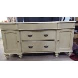 An early 20thC washed green painted pine serpentine front sideboard with three frieze drawers,