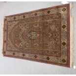 A Persian silk rug with dence floral decoration and a border of Arabic text, on a beige ground