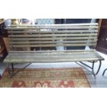 An early 20thC garden bench, the weathered teak slats raised on a wrought iron underframe with