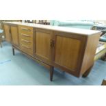 A 1970s teak sideboard with a central bank of four drawers, flanked by two pairs of doors, raised on