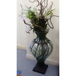 A modern metal bound glass floorstanding vase with a faux flower display  40"h overall