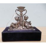 An early 20thC silver/white metal desktop taperstick holder, fashioned with two girls seated back-