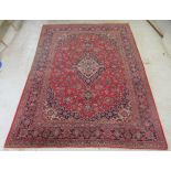 A Kashan carpet, decorated with a central diamond shaped motif, profusely bordered by floral and