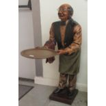 A 20thC composition menu stand, fashioned as a balding bespectacled gentleman holding a serving tray
