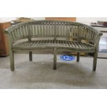 A modern teak garden bench of curved slatted design, raised on block legs  66"w