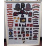 A framed display of woven and other military uniform badges and similar insignia, some copies: to