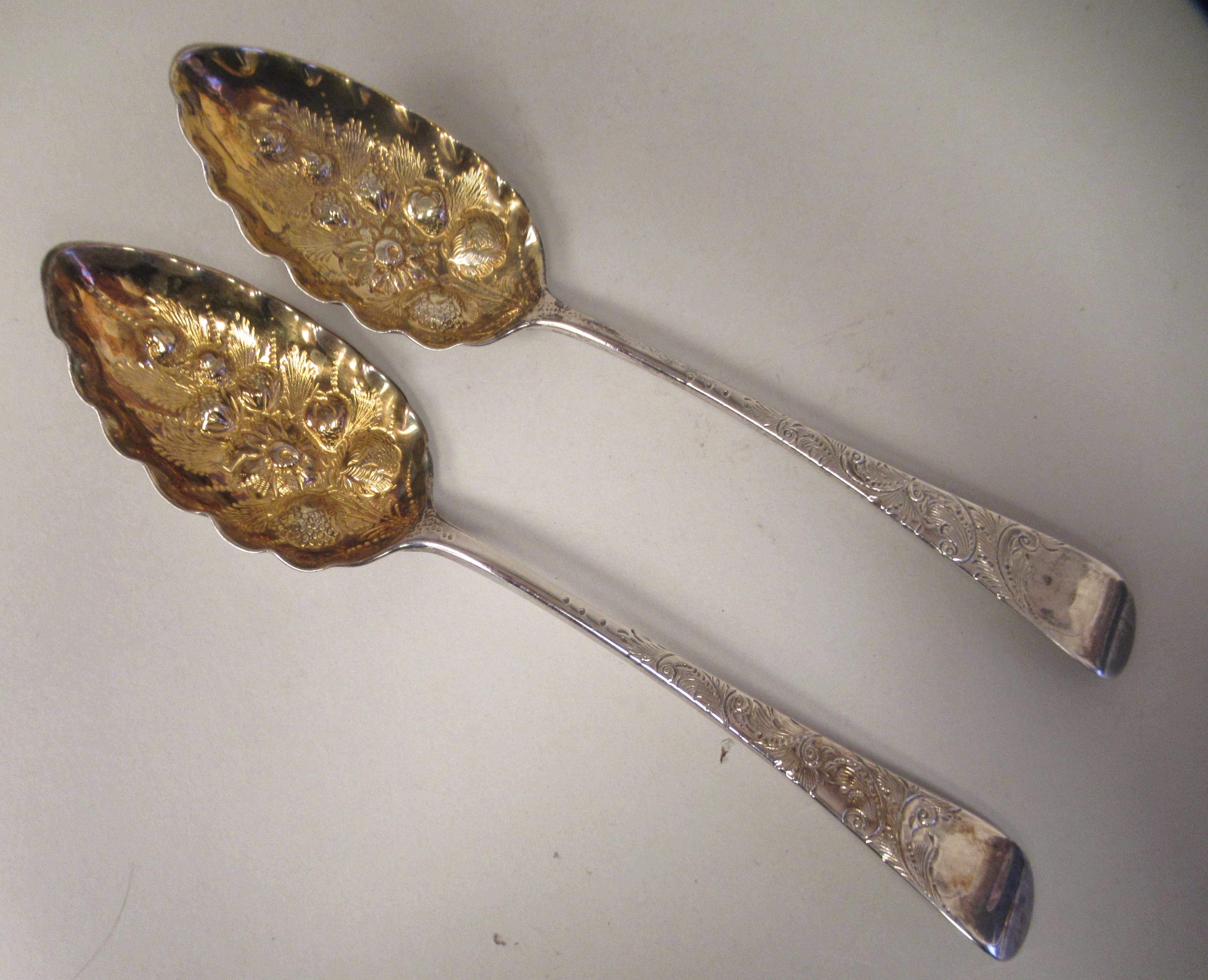 A pair of George III silver and parcel gilt Old English pattern berry spoons with foliate engraved