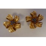 A pair of textured 18ct gold ribbon tied floral clip-on earrings, claw set with sapphires