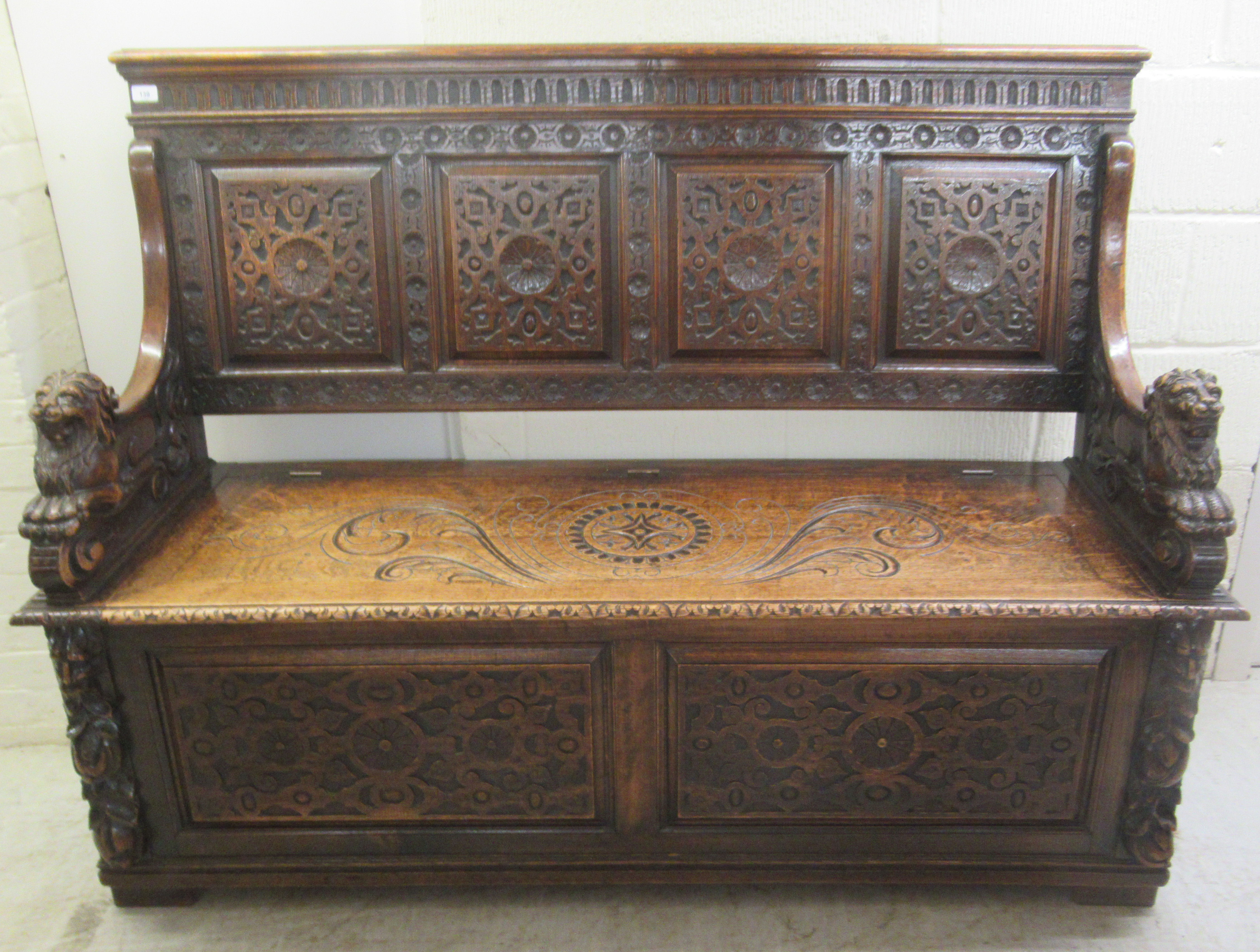 A late Victorian profusely carved oak settle with a high, level, quadruple fielded panelled back and