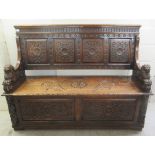 A late Victorian profusely carved oak settle with a high, level, quadruple fielded panelled back and