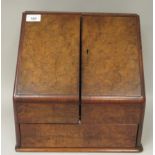 An early 20thC walnut veneered desktop stationary box, the cushion moulded, hinged top revealing a