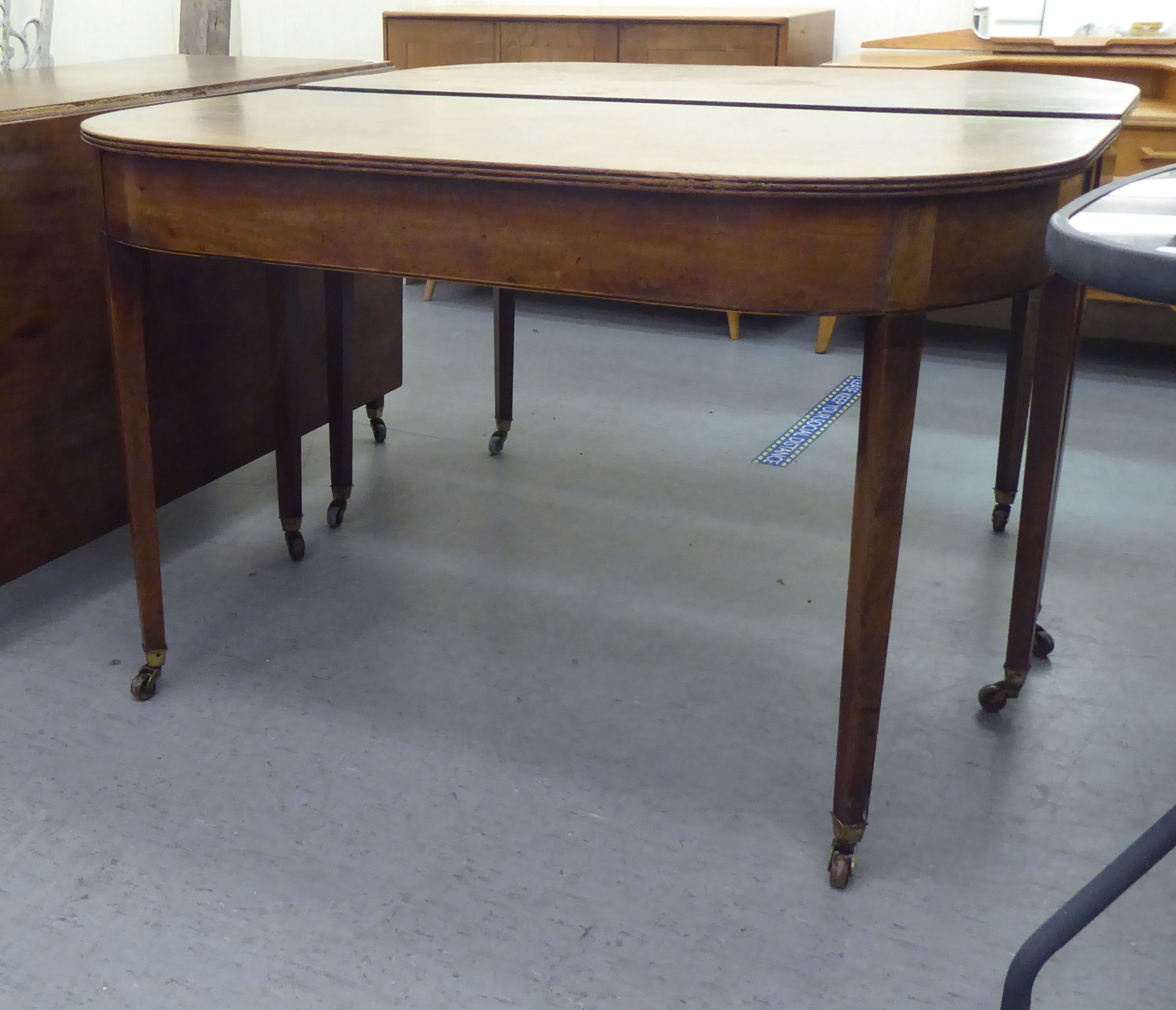 A George III mahogany dining table, comprising a drop leaf centre section and two D-ends, raised