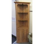 A waxed pine standing corner cupboard, the upper part with open shelves, over two panelled doors