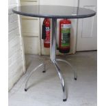 A modern chromium plated steel pedestal table with a black stone top, raised on a quadruped base