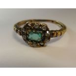 A yellow metal cluster ring, set with a central emerald, surrounded by diamonds (two missing)