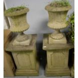 A pair of reconstituted stone urns on pedestals.