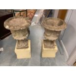 A pair of stone composite garden urn planters on sandstone bases.