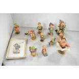 A collection of Goebel Hummel figures of children; and a needlework of a child.