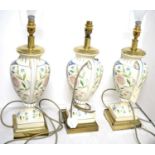 A set of three floral decorated twin-handled urn vase table lamps.