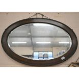 An oval bevelled wall mirror in carved dark oak frame