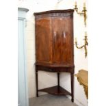 A mahogany serpentine front two door corner cabinet on stand