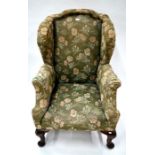 An upholstered Victorian wing armchair raised on mahogany legs