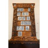 An Arts & Crafts foliate carved oak hymn board with silver painted numbered tiles, 55 cm wide x 87