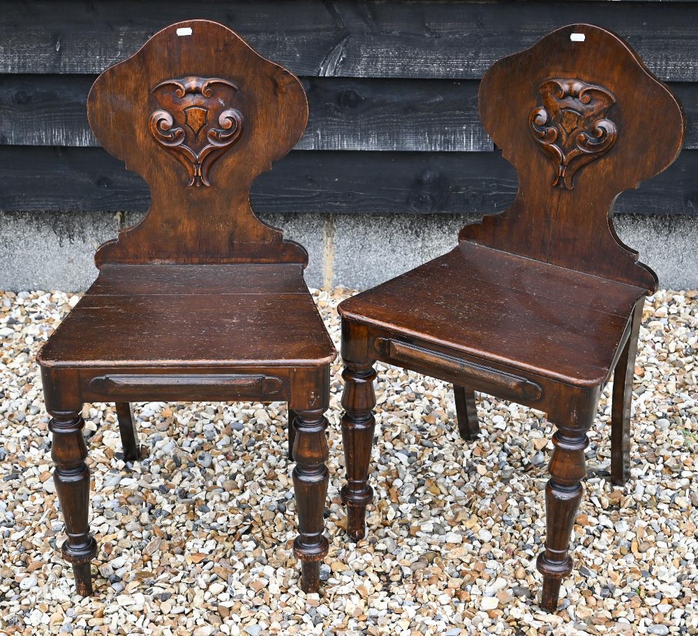 A pair of Victorian armorial carved oak hall chairs with panelled seats and turned front legs (2)