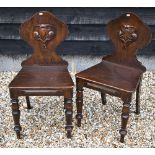 A pair of Victorian armorial carved oak hall chairs with panelled seats and turned front legs (2)