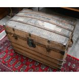A 1920s dome top canvas covered trunk with travel labels and stenciled ownership, wooden bands,