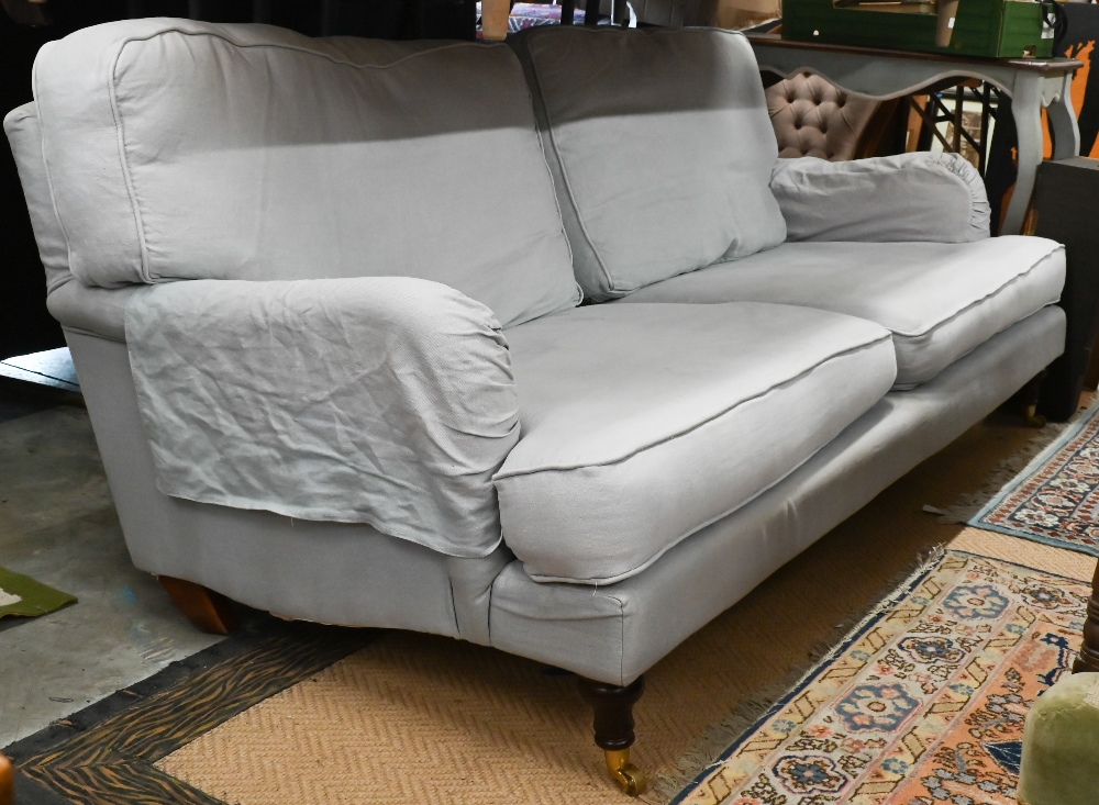 A Howard style three seater sofa, turned mahogany front legs with brass castors, pale blue