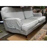 A Howard style three seater sofa, turned mahogany front legs with brass castors, pale blue