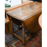 An early 20th century oak drop-leaf dining table on gateleg action with barley twist supports